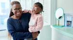 dr.consulta - Na imagem, mulher segura menina de, no máximo 2 anos, no colo que precisa usar óculos. As duas sorriem e usam óculos.