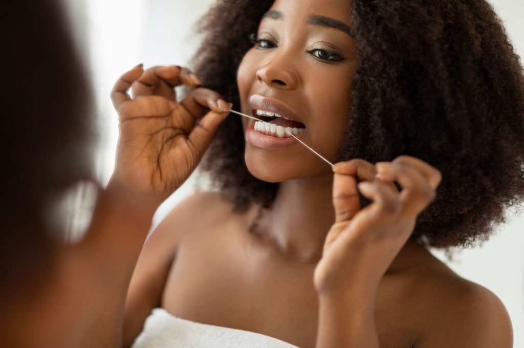 Mulher negra cuidando de sua saúde bucal ao passar fio dental nos dentes.