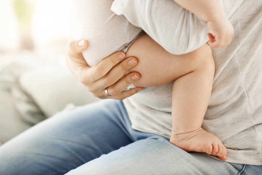 Imagem de uma pessoa segurando um bebê no colo. Nem o rosto da criança quando da pessoa adulta estão visíveis.