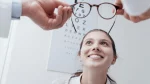 dr.consulta - Na imagem, óculos são movimentados em direção ao rosto de mulher por mãos de médicos. Atrás, letras usadas para teste de miopia.