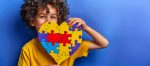 Criança sorridente segurando um coração feito de peças de quebra-cabeça coloridas, símbolo da conscientização sobre o autismo