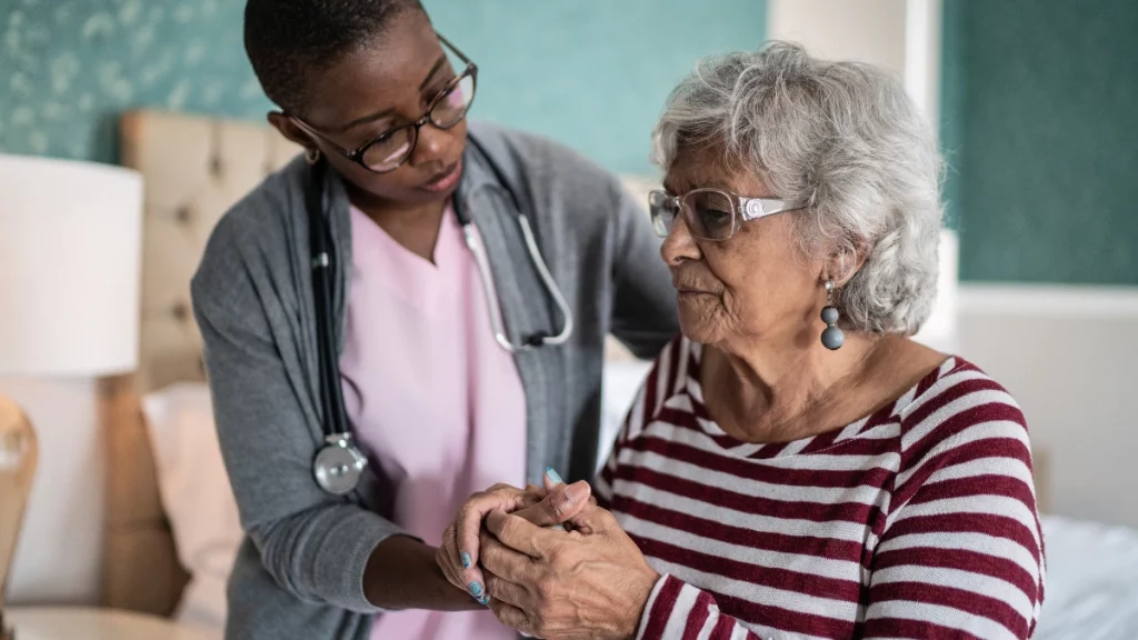 dr.consulta - Idosa com dificuldade para se manter em pé, um dos Sintomas do Parkinson, sendo auxiliada por uma profissional de saúde.