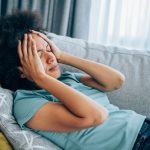 drconsulta - sintomas da anemia, mulher deitada no sofá com dor na cabeça, sintomas silenciosos, dores no corpo, enjoo