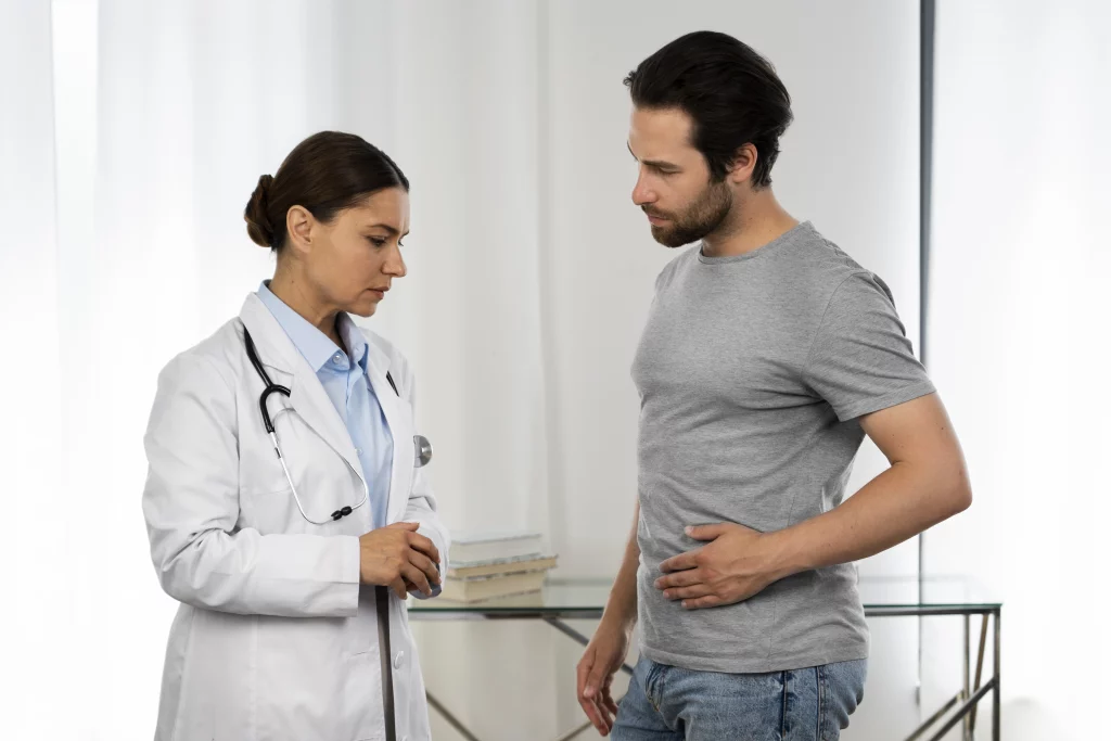 A imagem mostra um homem sendo atendido por uma profissional da saúde. Ele aparenta estar com incômodo na região abdominal.