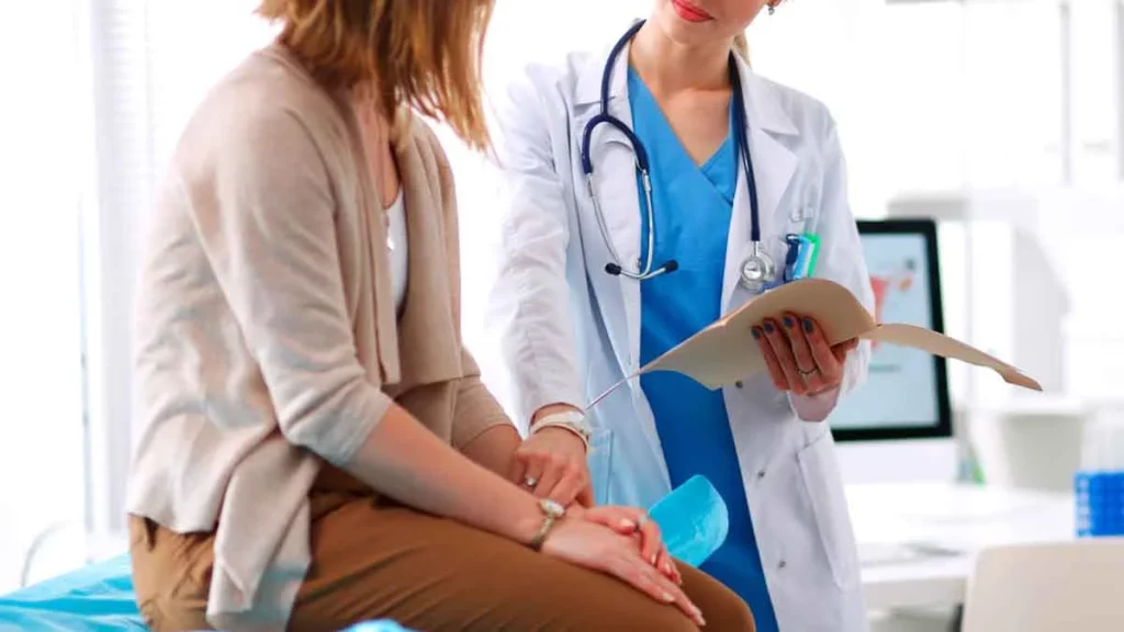 paciente está sentada em um consultório conversando com sua ginecologista, que segura uma pasta com resultados de exames