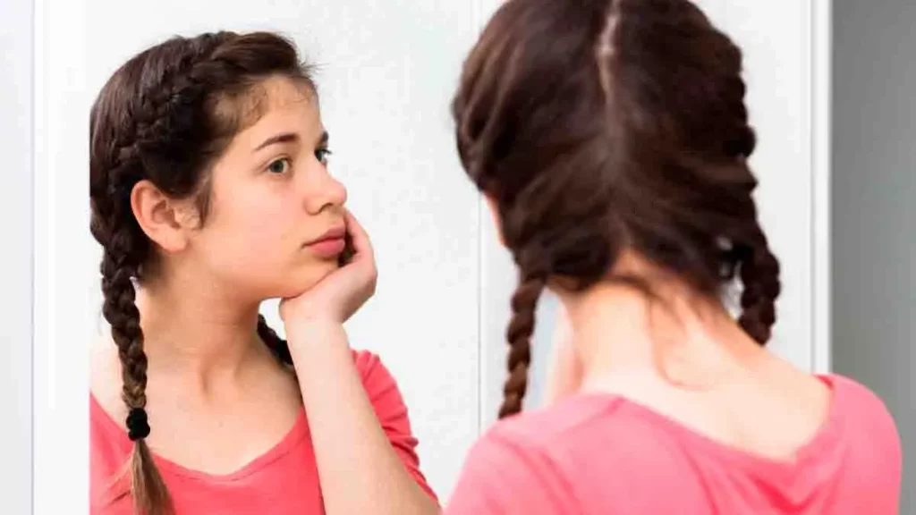 Menina de tranças e camiseta rosa se olhando no espelho