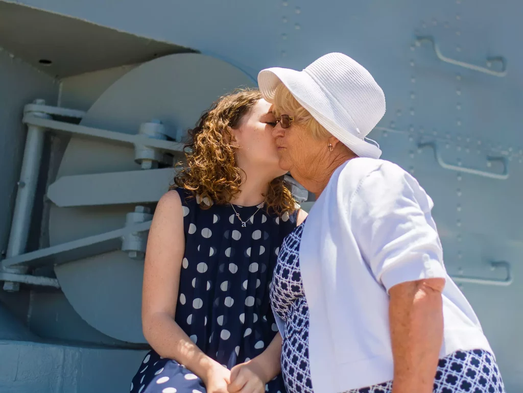 A foto mostra uma menina branca beijando o rosto de uma mulher idosa, provavelmente sua avó. 