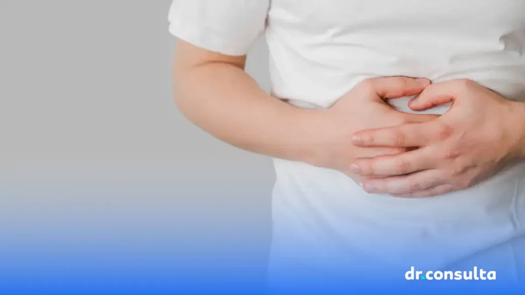 Na imagem é possível ver um homem branco de camisa também branca com as mãos sobre o abdômen como se sentisse dor. O rosto não aparece.