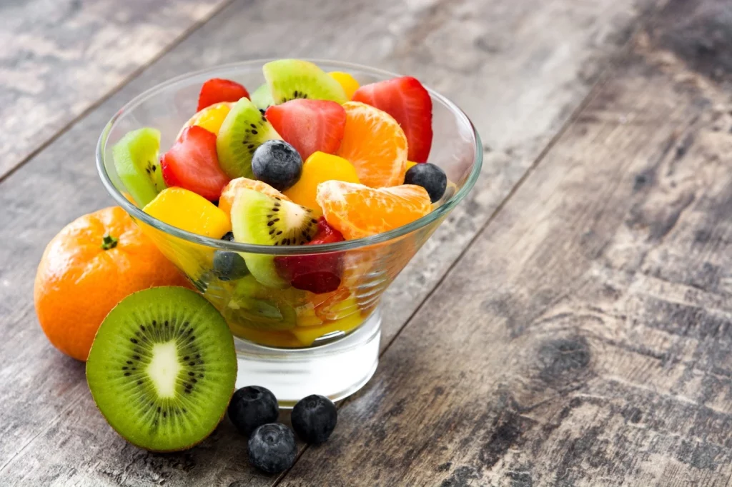 Taça de sobremesa de vidro cheia de frutas diversas. A taça está sobre uma mesa de madeira.