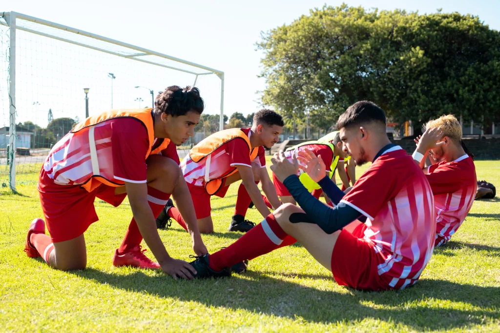 Imagem de um grupo de jovens, com uniformes de jogo, se aquecendo para um jogo de futebol em um campo aberto.