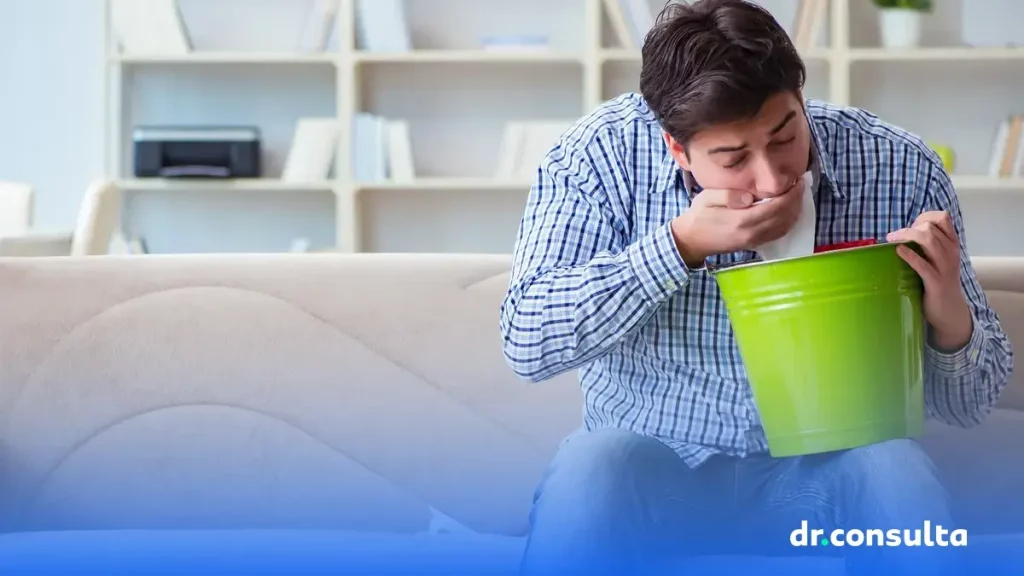 Na imagem, um homem com virose segura um balde enquanto se prepara para vomitar.