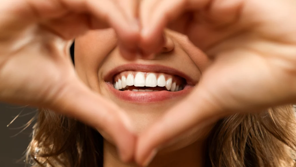 dr.consulta - mulher com sorriso branco, fazendo um coração com as mãos, feliz, clareamento dental, procedimentos estéticos bucais