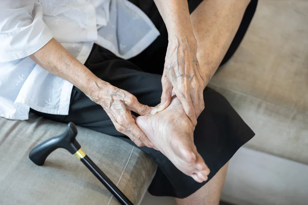 Imagem de uma idosa massageando os calcanhares. Seu rosto não está visível. 