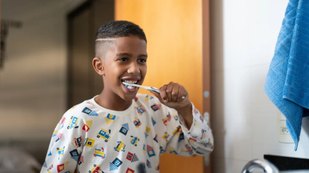 dr.consulta - quando procurar um dentista, criança negra, escovando os dentes em frente a um espelho, no banheiro de casa