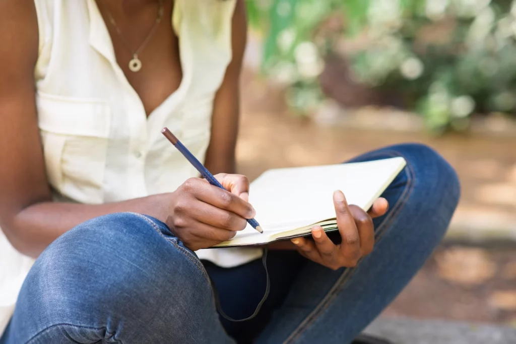 Imagem de uma mulher sentada anotando em um caderno algumas emoções – tarefa essa proveniente da Terapia Cognitivo Comportamental.