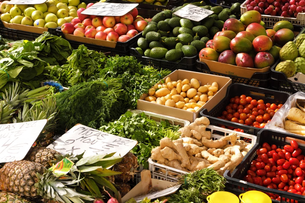 A imagem mostra várias opções de verduras, legumes e frutas coloridos expostas em caixas de feira.