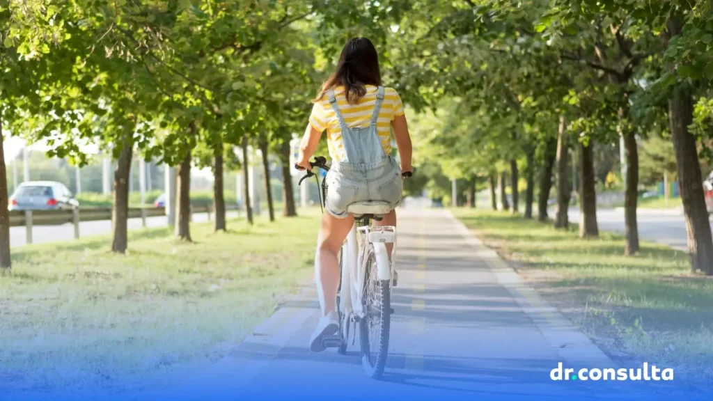 Imagem de uma mulher andando de bicicleta de costas, em uma rua com árvores de ambos os lados.