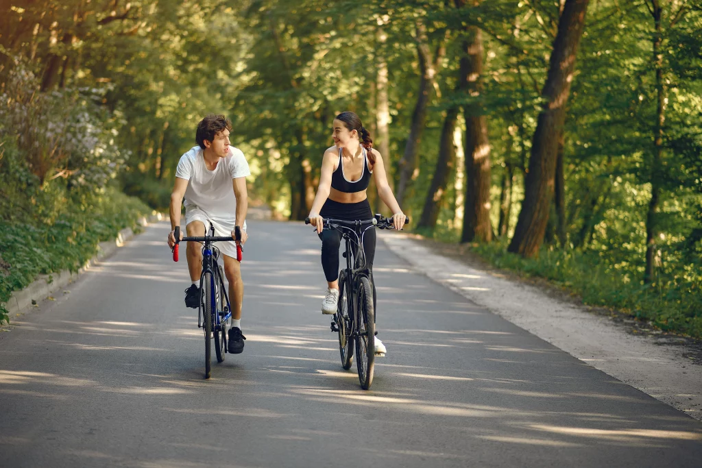 Imagem de uma mulher e um homem andando de bicicleta em uma rua envolta de árvores.