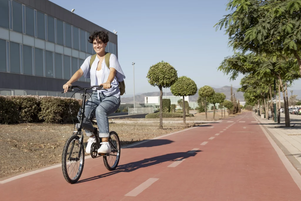 Imagem de uma mulher, que aparenta ser uma estudante, andando de bicicleta em uma ciclovia Ela está de frente e sorrindo.