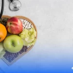 A imagem mostra uma bandeja com frutas, verduras e grãos. Na imagem também há uma garrafa de água com tampa laranja e um estetoscópio.