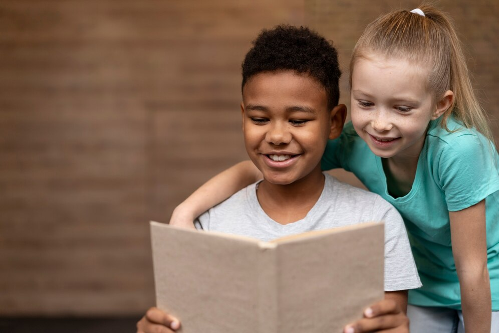 Imagem de duas crianças, um menino e uma menina, lendo um livro juntos. Ambos estão olhando para as páginas e sorrindo.