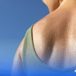 A imagem mostra as costas de uma mulher, de blusa verde. A região apresenta gotículas de água que representam suor.