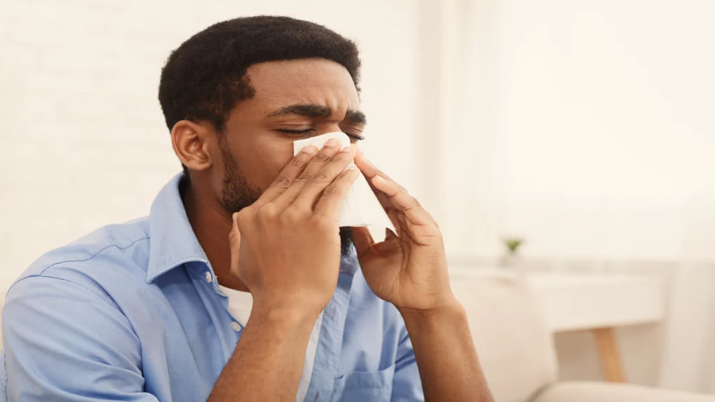 Imagem de um homem negro assoando o nariz com um lenço branco de papel.