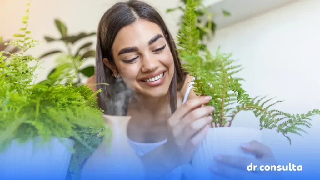 Imagem de uma mulher sorrindo e cuidando de plantas em casa. Além disso, é possível ver um umidificador de ar.