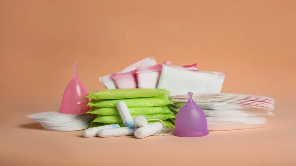 Imagem de vários tipos de absorventes menstruais com embalagens cor de rosa, verde e roxa.