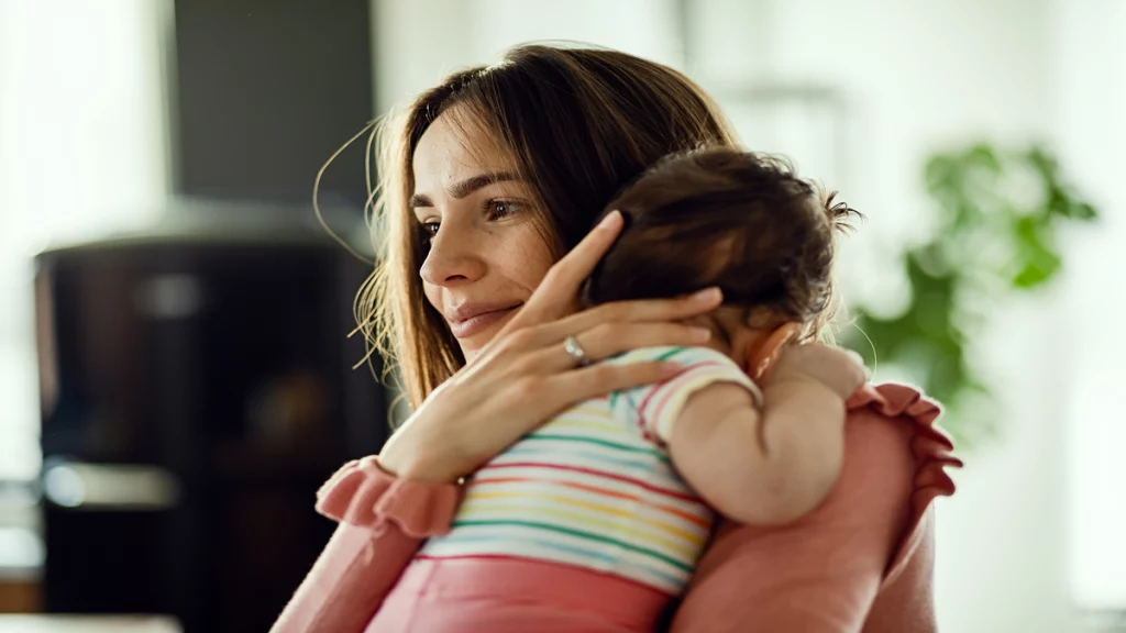 Imagem de uma mãe segurando sua filha bebê. O rosto da criança não aparece na imagem.