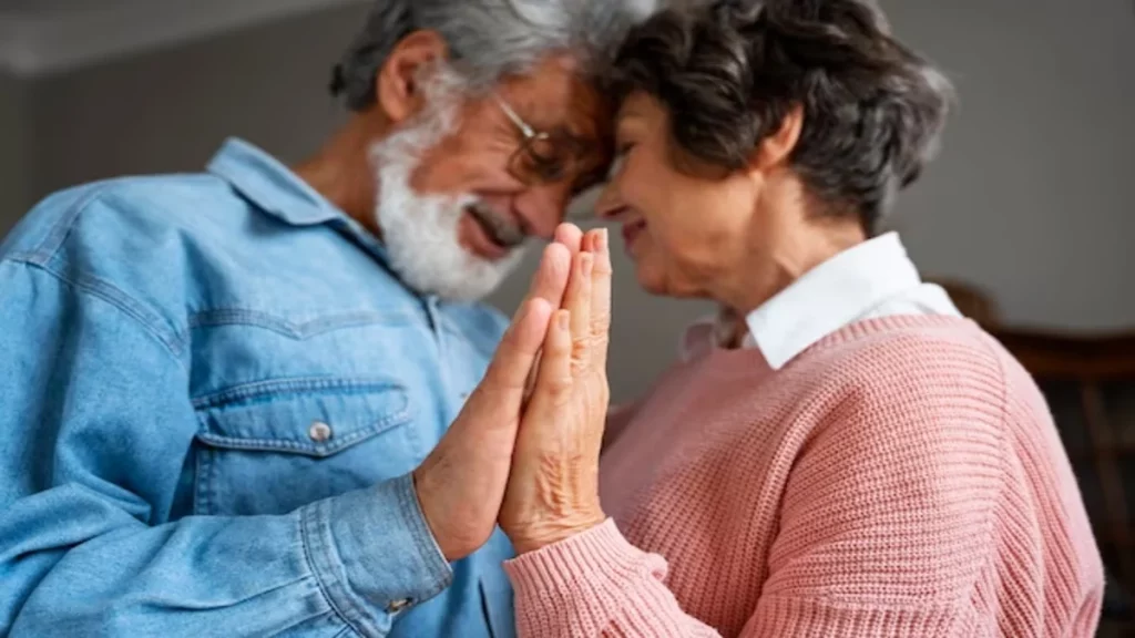 Imagem de um casal da terceira idade tocando as mãos. Eles estão com o rosto próximo um do outro e sorrindo.