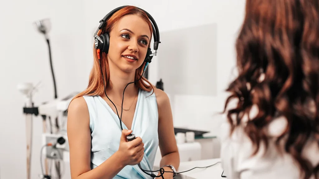 dr.consulta - mulher jovem, usando equipamento específico para exame de audiometria, sinaliza clicando no botão cada som que consegue escutar