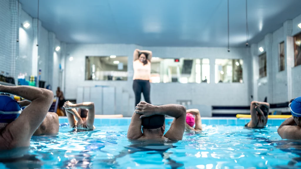 dr.consulta - pessoas na piscina fazendo aula de hidroginástica seguindo as orientação de uma professora que está na borda da piscina, atividades físicas para o bem-estar