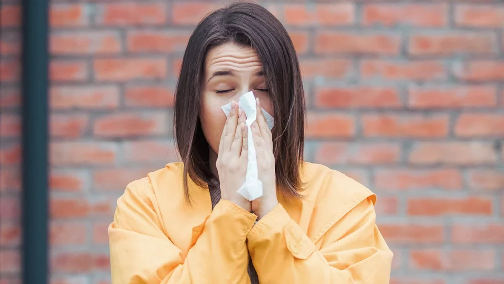 mulher jovem, usando agasalho amarelo, demonstra estar com coriza; vírus sincicial respiratório