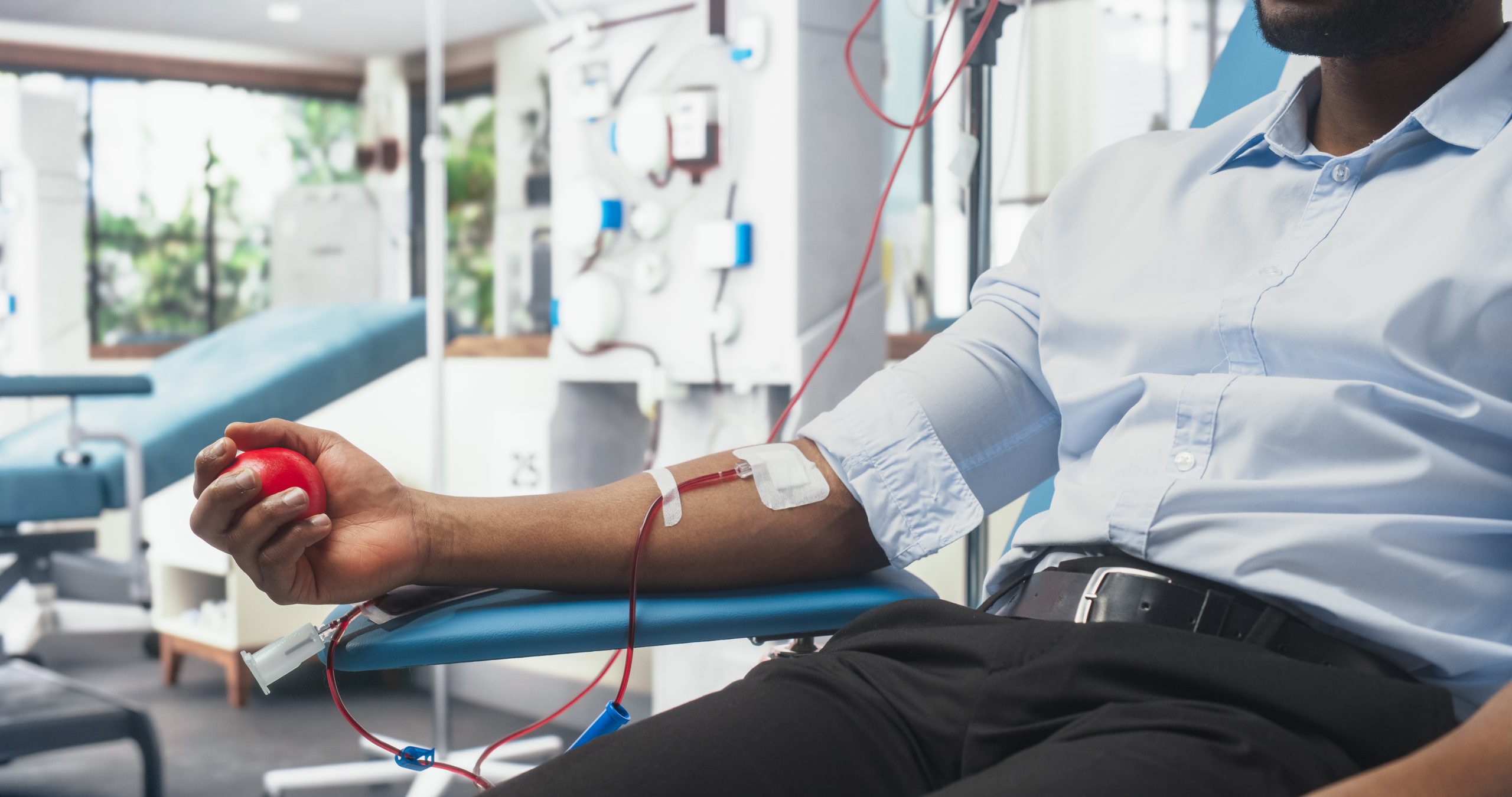 Homem doando sangue em clínica, segurando bola vermelha para estimular a circulação durante coleta