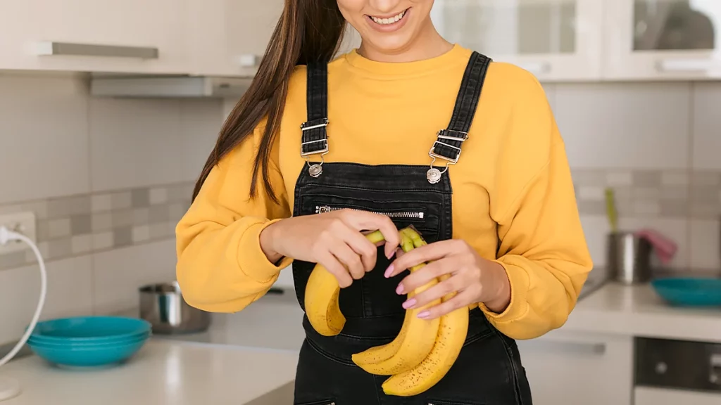 dr.consulta - jovem em uma cozinha com uma penca pequena de bananas nas mãos, separando para comer, benefícios da banana para a saúde, frutas no cardápio, alimentação