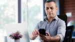 dr.consulta - Homem segurando o smartphone com os braços esticados. A dificuldade para ler a tela é um sinal da vista cansada