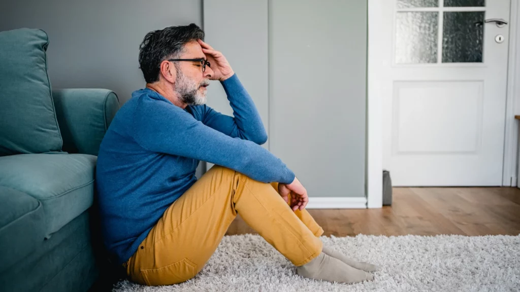 dr.consulta - Hmem com sintomas de depressão sentado no chão da sala, em frente ao sofá.