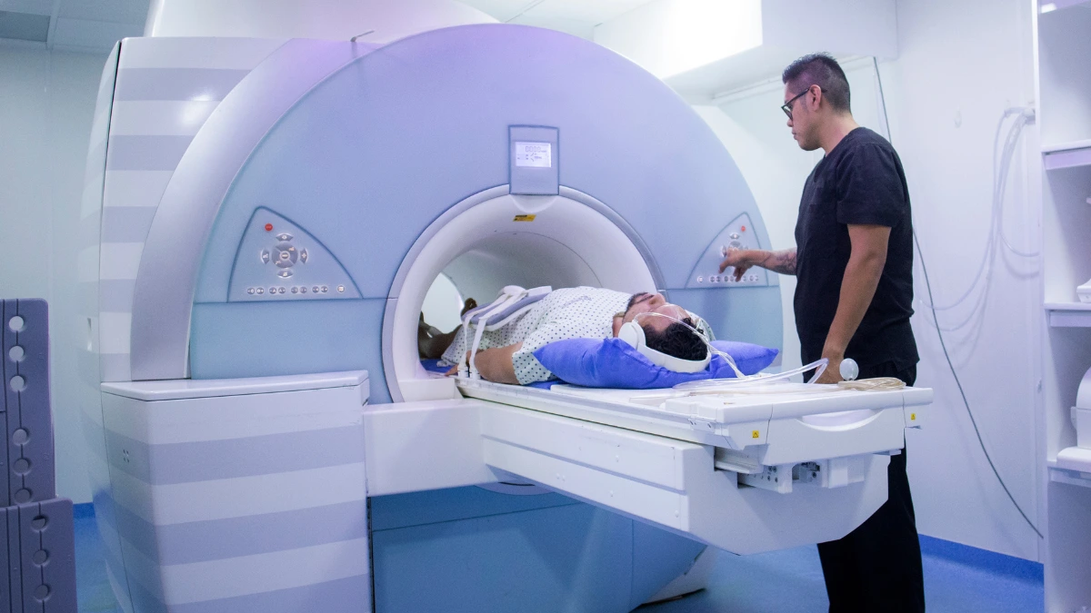 dr.consulta - Na imagem, enfermeiro conduz paciente em exame de colangiorressonância. Para isso, homem está deitado em maca, dentro de aparelho de ressonância magnética.