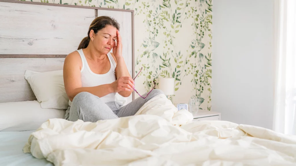 dr.consulta - Mulher branca com idade avançada passando mal e sentada na cama. Ela está com o edredom romovido para tentar reduzir o efeito da menopausa, como o suor noturno.