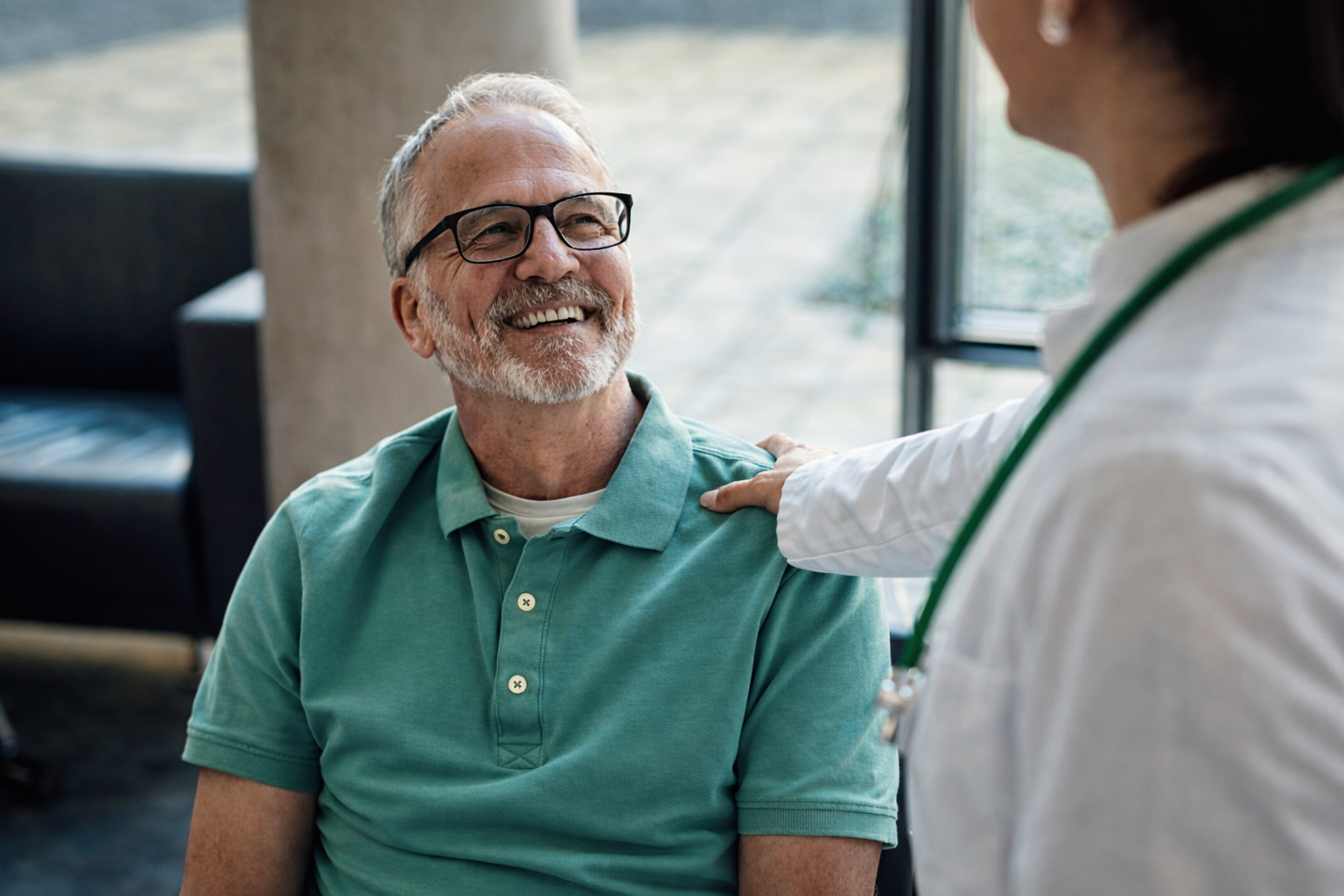 Homem idoso sorrindo durante consulta médica com profissional de saúde, representando cuidado e prevenção na saúde do homem